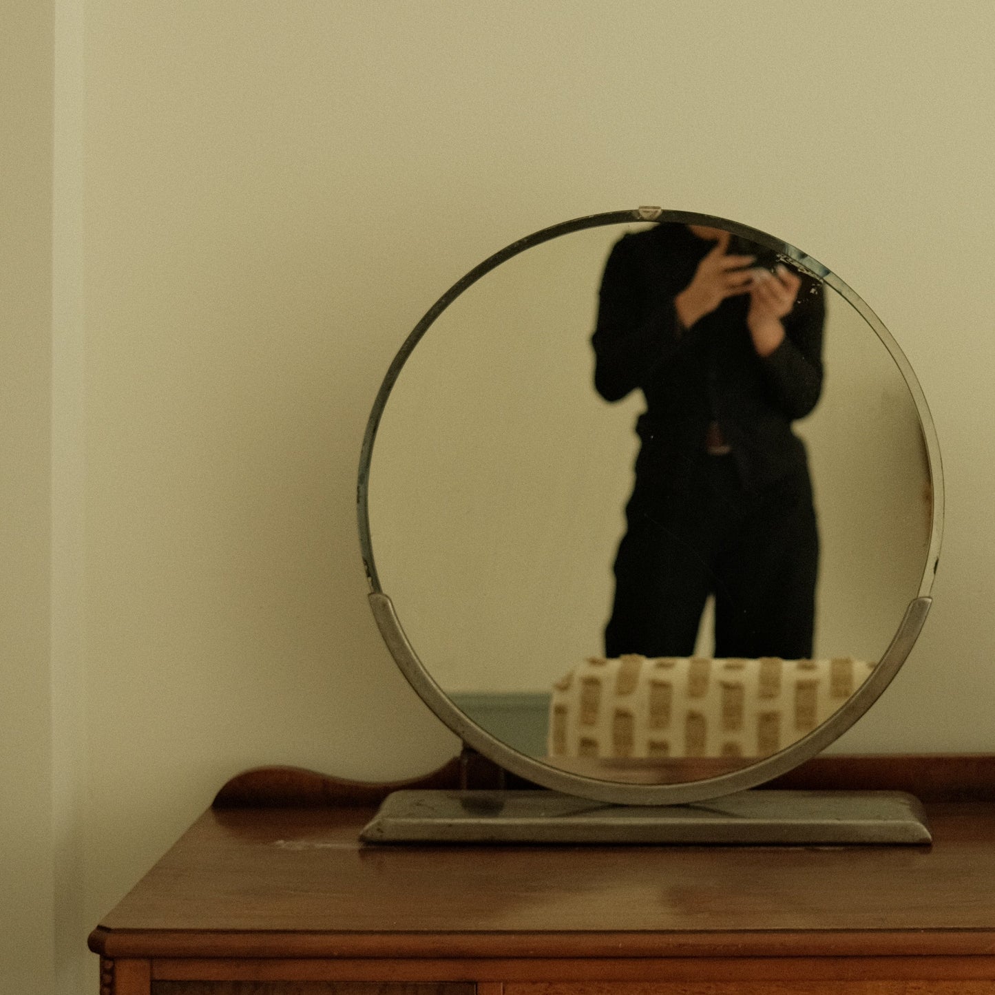 Person taking a mirror selfie in a room with a wooden cabinet and decorative items.