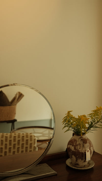 Round mirror on a stand with a vase of flowers against a beige wall