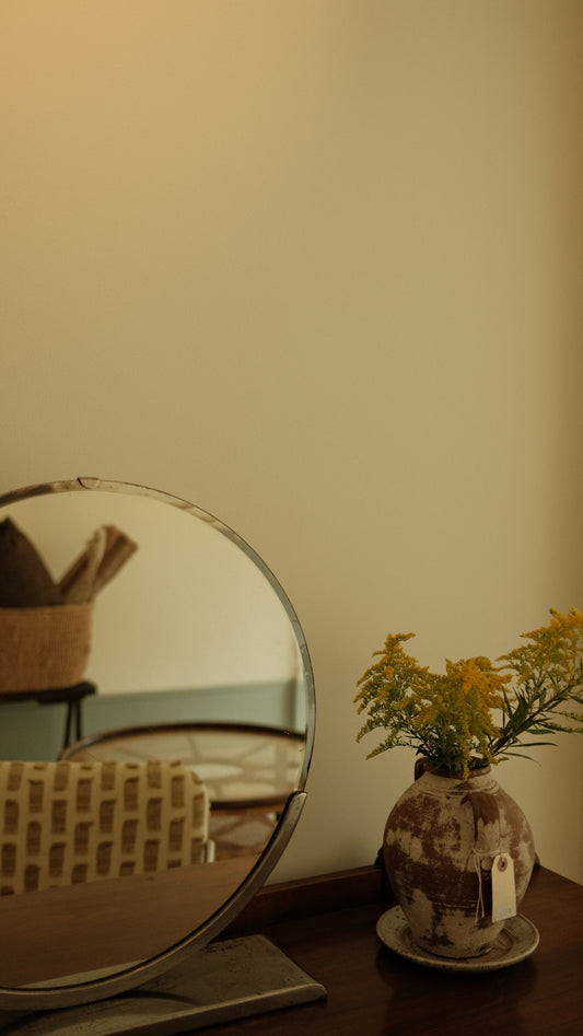 Round mirror on a stand with a vase of flowers against a beige wall