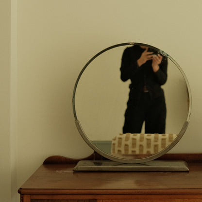 Person taking a mirror selfie in a room with a wooden cabinet and decorative items.